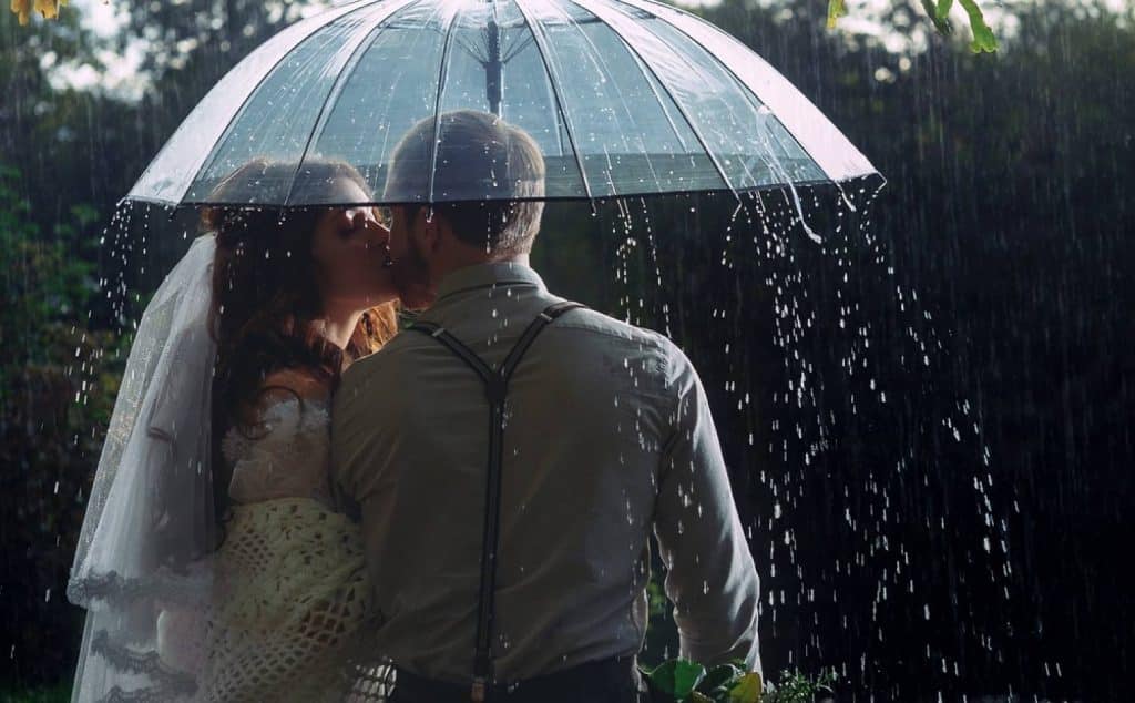 un marié et une mariée sous un parapluie pendant qu'il pleut